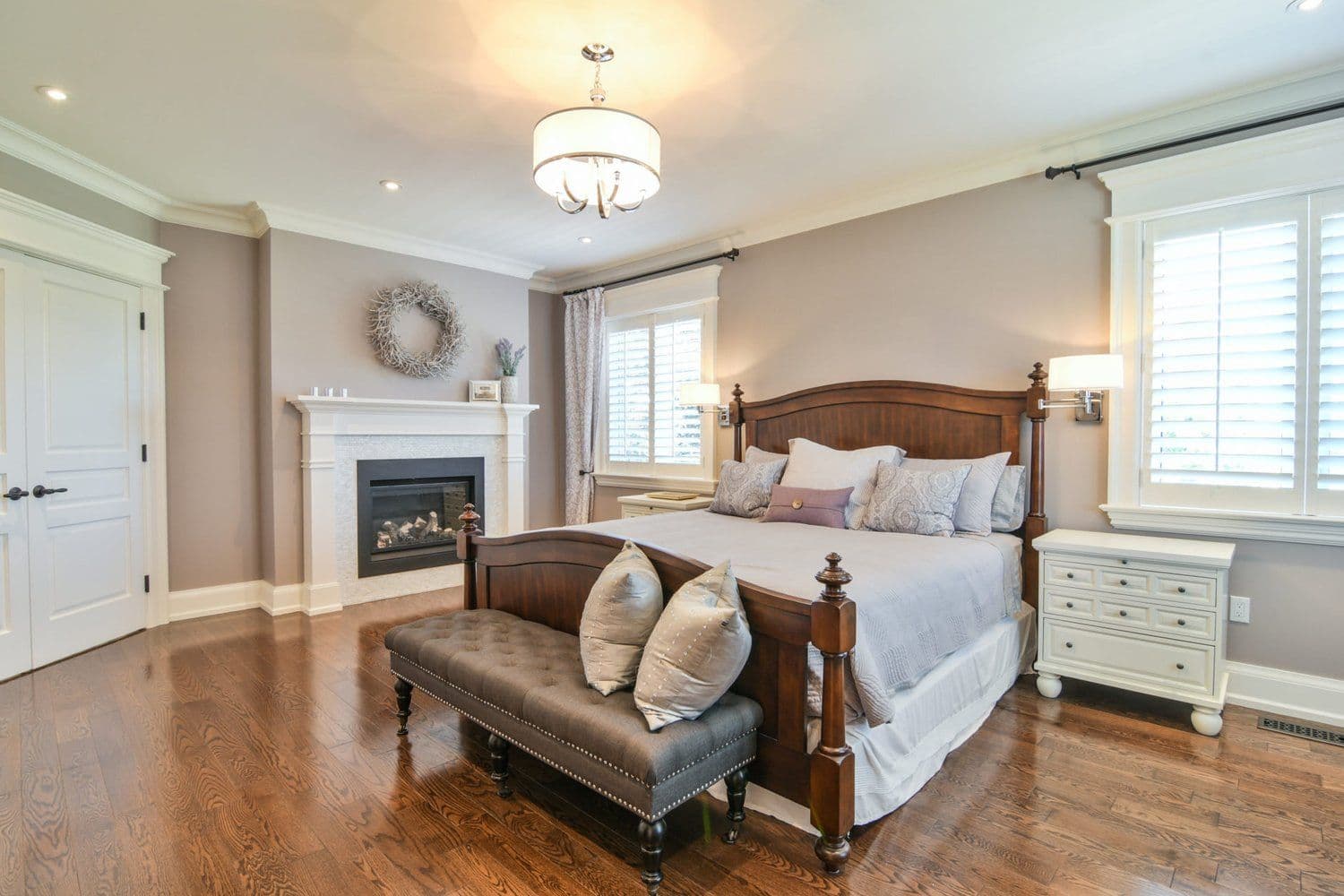 Primary bedroom with fireplace, upholstered bench and shuttered windows in a Creek Road custom home